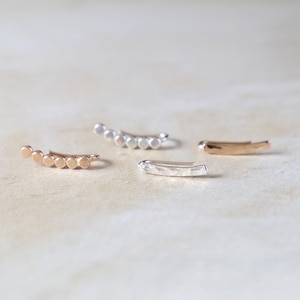 May include: Four ear cuffs in different styles. Two are made of gold metal and have a curved shape with small round beads. One is a silver ear cuff with a curved shape and small round beads. The other is a silver ear cuff with a straight shape.