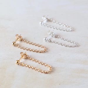 May include: Three pairs of chain earrings with a small ball at the end of each chain. The earrings are shown in gold, silver, and a combination of gold and silver.