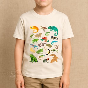 May include: A cream-coloured t-shirt with a vibrant illustration of reptiles and amphibians. The design includes a yellow chameleon, green iguana, and a brown crocodile. The shirt is made of a soft material.