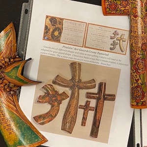 May include: A tutorial for creating gourd crosses. The image shows three different gourd crosses, each with intricate details and a unique design. The text on the page reads "Praisin' Art Gourd Cross Tutorial".