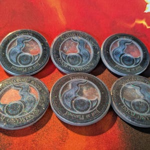 May include: Six round game tokens with a blue and orange design. The tokens have the words "COMMAND POINT" and "Just as Planned" around the edges. The center design features a stylized flame or bird-like shape.