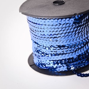 May include: A spool of blue sequin trim. The trim is made of small, round sequins that are sewn together in a continuous line.
