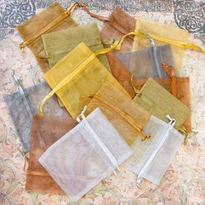 Peut inclure: Un ensemble de petits sacs en organza transparent de différentes couleurs, dont l'or, le brun et le gris. Les sacs sont faits d'un tissu délicat et translucide et ont une fermeture à cordon.