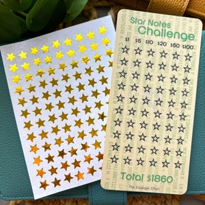 May include: A teal leather wallet holds a gold star sticker sheet and a "Star Notes Challenge" card. The card has star outlines for tracking savings goals, with amounts from $1 to $100. The total savings goal is $1860.