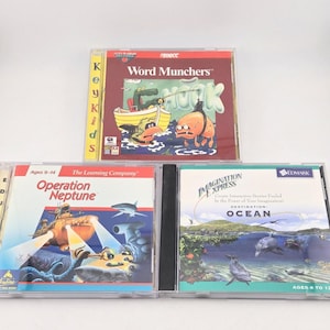 May include: Three vintage computer game CD-ROM cases including Word Munchers, Operation Neptune, and Imagination Express Destination: Ocean. Each case features colorful graphic cover art with titles, age ratings, and publisher logos clearly visible.