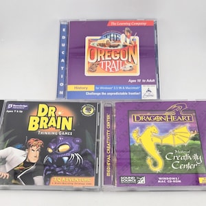 May include: Three computer game CD-ROM cases featuring The Oregon Trail, Dr. Brain Thinking Games, and DragonHeart Medieval Creativity Center. Each case displays colorful cover art, game titles, and system compatibility information for Windows and Mac.