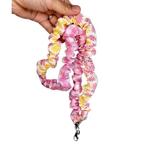 May include: A fabric lanyard featuring a gathered, scrunchie-style design. The textile displays a pattern of pink and yellow daisy flowers on a white background, alternating with sections of a pink and white gingham checkered fabric pattern.