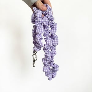 May include: A lavender and white gingham fabric lanyard with a silver-colored clasp and key ring. The lanyard is held up against a white background.