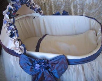 May include: A white wicker bassinet with a white and blue floral trim, a white and blue satin bow, and a white tulle skirt.