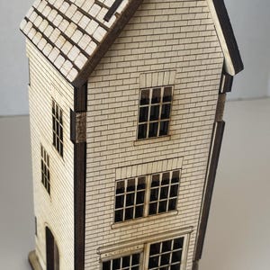 May include: A detailed wooden model of a house, featuring a brick-effect facade, a tiled roof, and dark brown detailing. The model includes windows, a front door, and a chimney. The measurements are in centimeters.