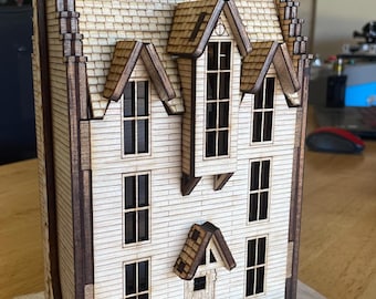 Könnte beinhalten: Ein Holzmodell eines Hauses mit braunem Dach, weißer Verkleidung und mehreren Fenstern. Das Haus hat eine kleine Veranda mit einer Tür und einem Fenster. Das Modell steht auf einem Holzsockel.