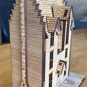 May include: A wooden model of a house with a tall chimney and a gabled roof. The house is made of laser-cut wood and has a detailed exterior.