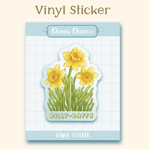 May include: A vinyl sticker featuring a cluster of yellow daffodils with green leaves and the text "DILLY-DAFFS" in a light blue banner. The sticker is on a blue and white grid background with the text "Dandy Doodles" and "Vinyl Sticker" in white.