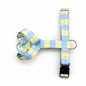 May include: A dog harness in a blue and yellow plaid pattern. The harness has a black buckle, metal rings, and adjustable straps. The brand name "4GRAMS" is printed on the harness.