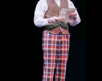 May include: A man in a stage costume stands holding a paper. He wears a white dress shirt, brown vest, and plaid pants with red, blue, and brown squares. Brown leather shoes and a red bow tie complete the look.