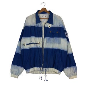 May include: A blue and white striped jacket with a full zipper closure. The jacket has a collared neckline, two front pockets, and a drawstring at the waist. The jacket has the word "pro" printed on the collar.