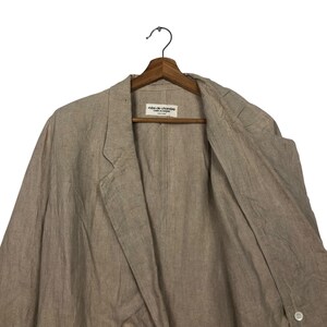 K&ouml;nnte beinhalten: Ein hellbeiger Blazer aus Leinen mit einem einzigen Knopfverschluss. Der Blazer hat ein Etikett mit der Aufschrift "robe de chambre" in der Mitte der Vorderseite.