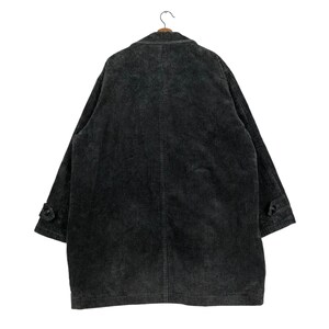 May include: A dark gray corduroy coat hangs on a wooden hanger. The coat has a classic design with a notched lapel, buttoned cuffs, and a long, relaxed fit. The corduroy fabric has a vertical ribbed texture.