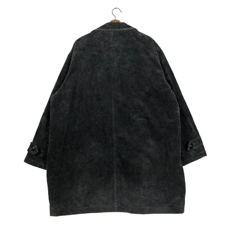 May include: A dark gray corduroy coat hangs on a wooden hanger. The coat has a classic design with a notched lapel, buttoned cuffs, and a long, relaxed fit. The corduroy fabric has a vertical ribbed texture.
