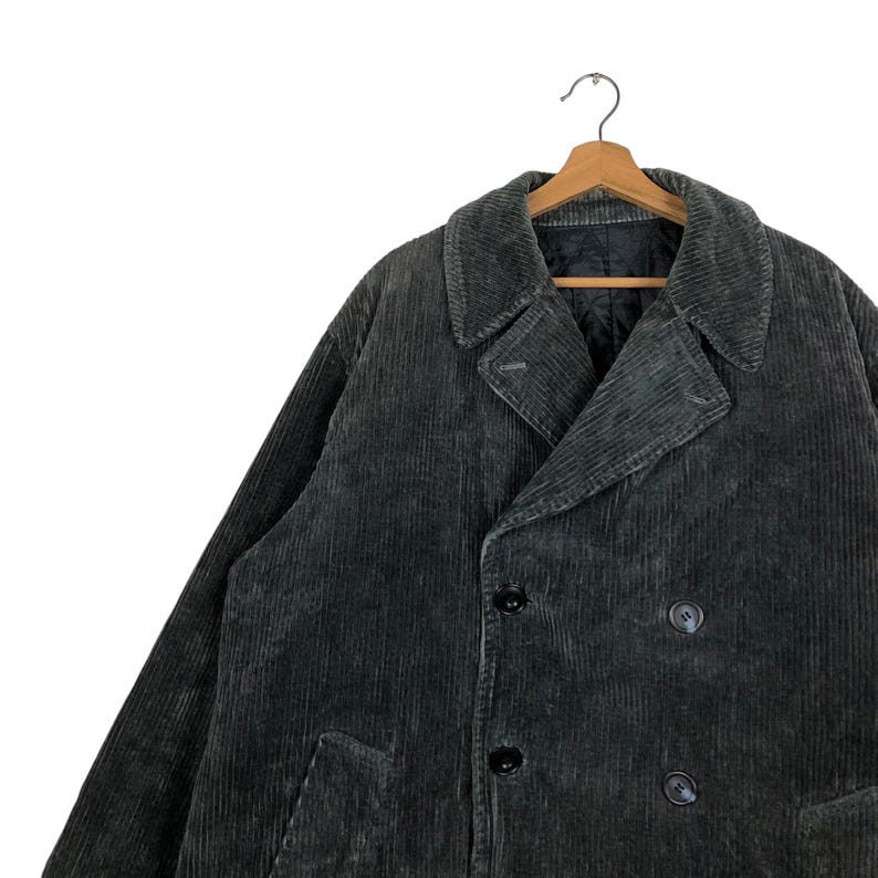 May include: A dark gray corduroy coat with a double-breasted design. The coat features a notched lapel, two rows of buttons, and a classic, tailored fit. The coat is hanging on a wooden hanger.