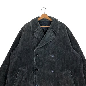 May include: A dark gray corduroy coat with a double-breasted design, featuring large lapels and black buttons. The coat is hanging on a wooden hanger against a white background. The fabric has a ribbed texture.