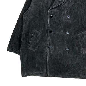 May include: A dark gray corduroy jacket with a double-breasted design. The jacket features a notched lapel, two front pockets, and black buttons. The fabric has a ribbed texture.