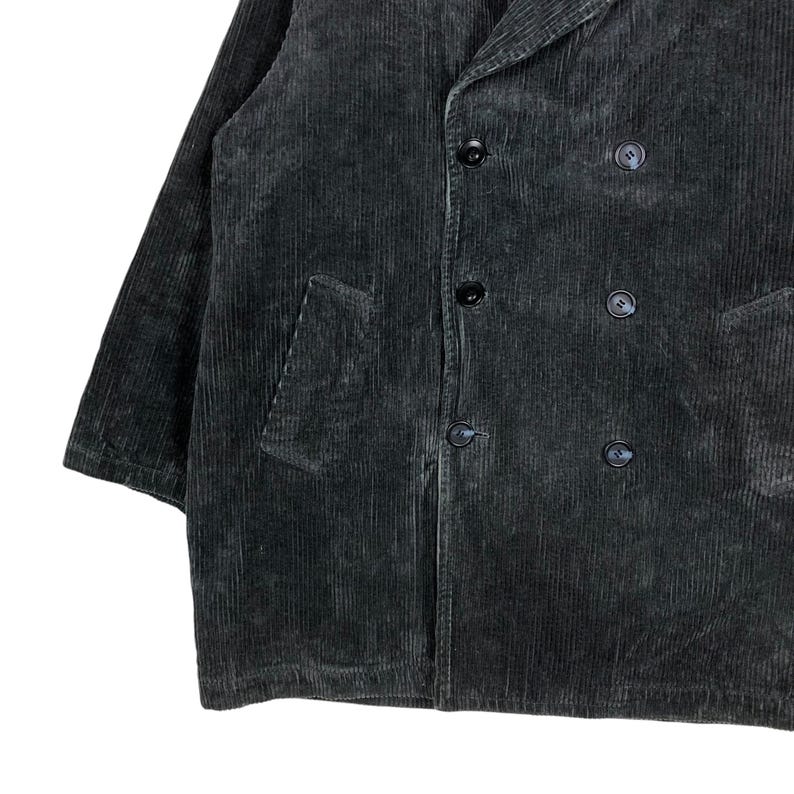 May include: A dark gray corduroy jacket with a double-breasted design. The jacket features a notched lapel, two front pockets, and black buttons. The fabric has a ribbed texture.