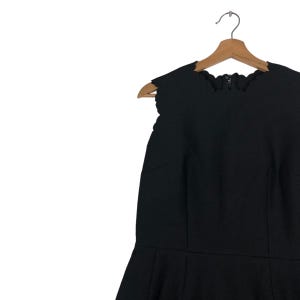 Puede incluir: Vestido negro sin mangas con escote festoneado y corpi&ntilde;o entallado. El vestido cuelga de una percha de madera. Tiene cierre de cremallera y falda acampanada.