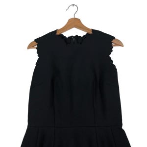 Puede incluir: Vestido negro sin mangas con escote festoneado y falda acampanada, colgado de una percha de madera. El vestido presenta cierre de cremallera en la espalda y un corpi&ntilde;o entallado. El dise&ntilde;o es elegante y adecuado para ocasiones formales. Mide unos 100 cm de largo.