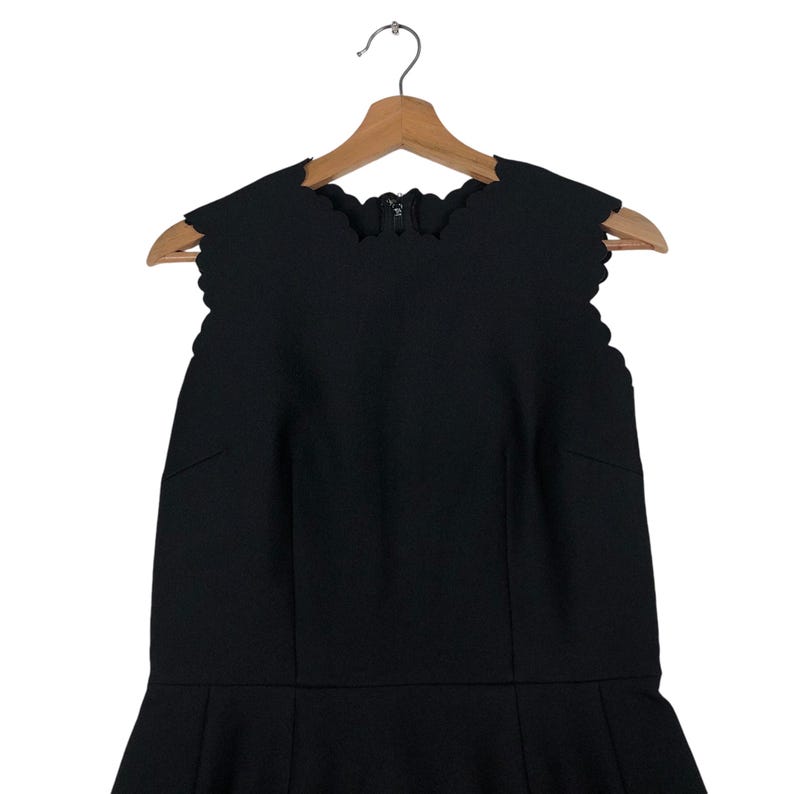 Puede incluir: Vestido negro sin mangas con escote festoneado y falda acampanada, colgado de una percha de madera. El vestido presenta cierre de cremallera en la espalda y un corpi&ntilde;o entallado. El dise&ntilde;o es elegante y adecuado para ocasiones formales. Mide unos 100 cm de largo.