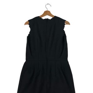 Puede incluir: Vestido negro sin mangas con escote y dobladillo festoneados, colgado de una percha de madera. El vestido tiene costuras verticales y una silueta entallada, lo que sugiere un dise&ntilde;o cl&aacute;sico.