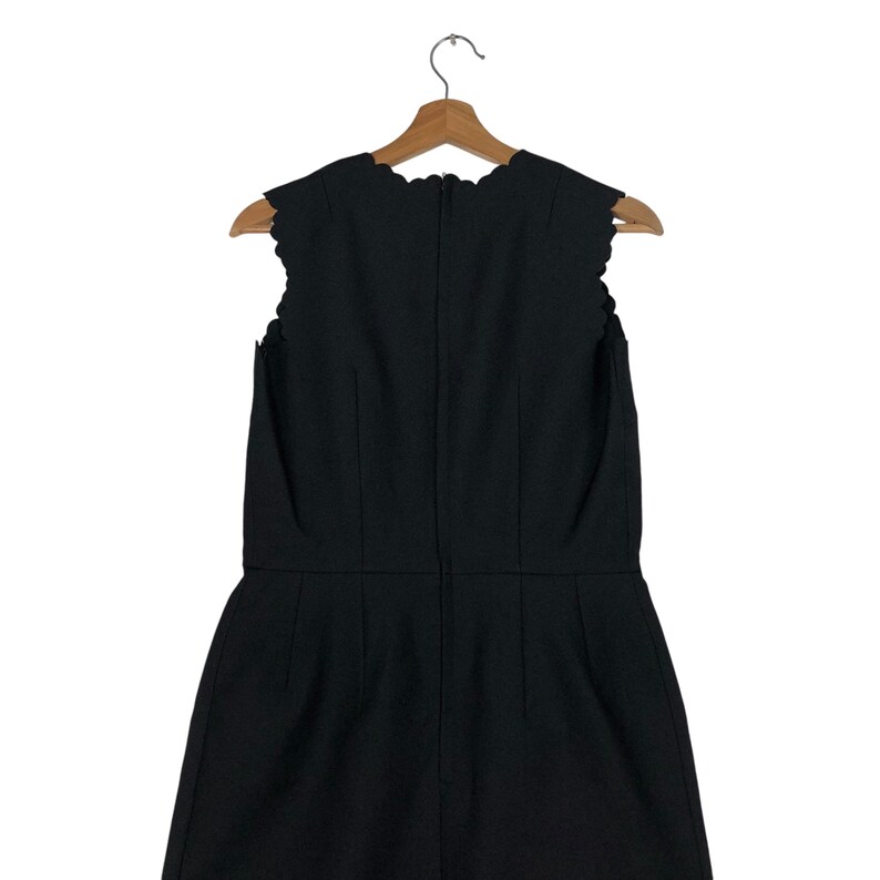 Puede incluir: Vestido negro sin mangas con escote y dobladillo festoneados, colgado de una percha de madera. El vestido tiene costuras verticales y una silueta entallada, lo que sugiere un dise&ntilde;o cl&aacute;sico.