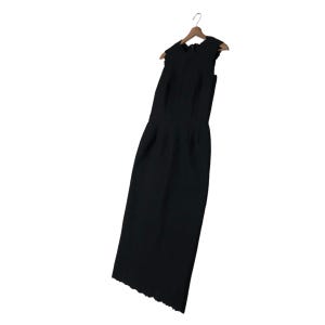 Puede incluir: Un vestido negro sin mangas con dobladillo festoneado, colgado de una percha de madera. El vestido tiene un corpi&ntilde;o ajustado y una falda recta. La tela del vestido es texturizada.