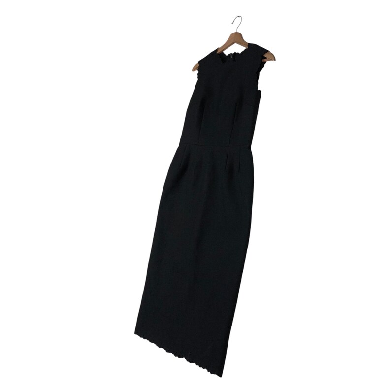 Puede incluir: Un vestido negro sin mangas con dobladillo festoneado, colgado de una percha de madera. El vestido tiene un corpi&ntilde;o ajustado y una falda recta. La tela del vestido es texturizada.