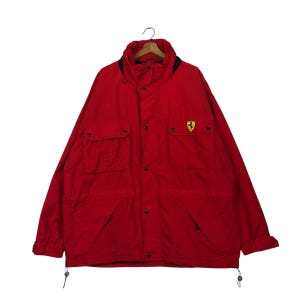 May include: A vibrant red jacket featuring a black collar and the Ferrari emblem on the chest. The jacket includes multiple pockets, a button-up front, and drawstrings at the hem. The jacket is a medium size.