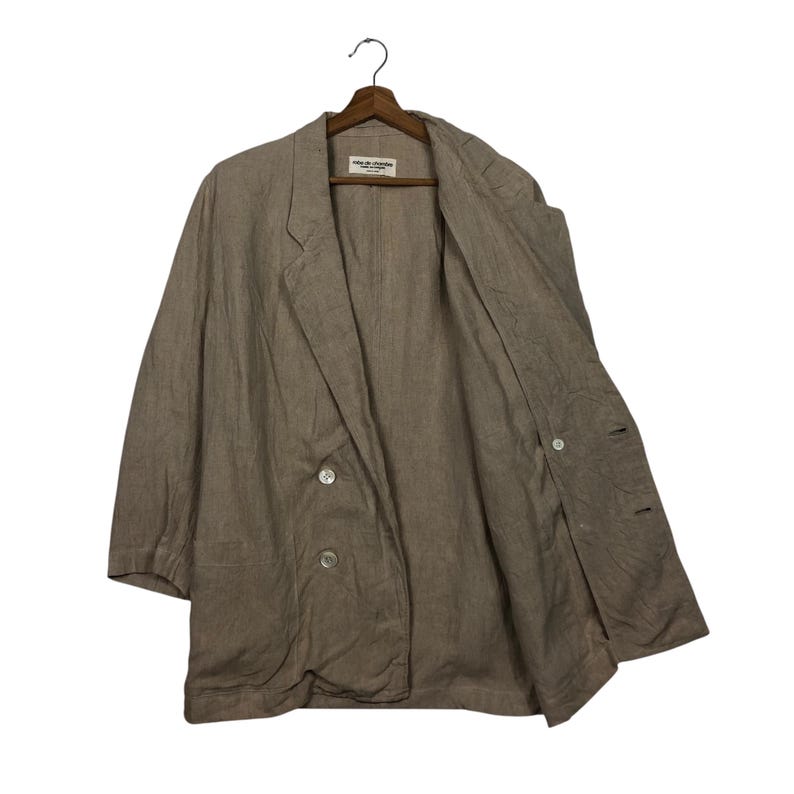 K&ouml;nnte beinhalten: Ein hellbrauner Blazer aus Leinen mit doppelreihigem Verschluss und zwei Kn&ouml;pfen. Der Blazer hat eine lockere Passform und eine leicht &uuml;berdimensionierte Silhouette. Das Etikett auf der Innenseite des Blazers lautet "Made in Canada".