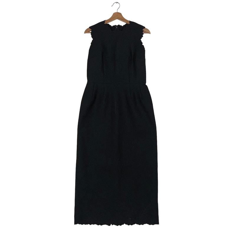 Puede incluir: Vestido negro sin mangas con escote y dobladillo festoneados, colgado de una percha de madera. El vestido tiene un corpi&ntilde;o ajustado y una falda recta, adecuado para ocasiones formales.