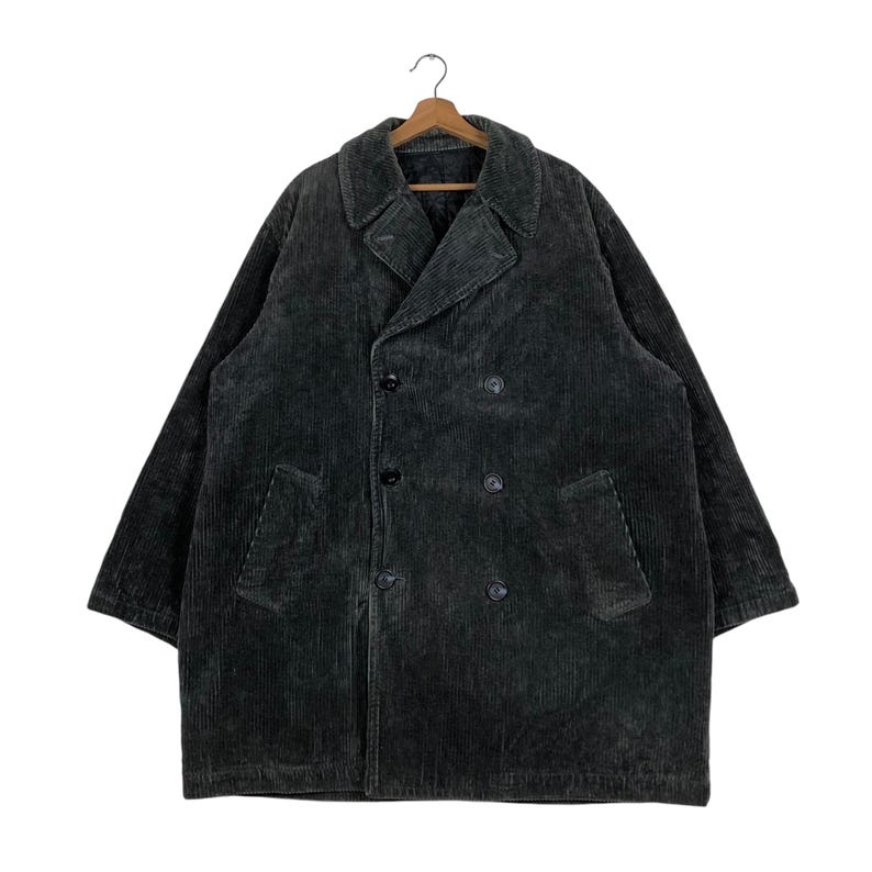 May include: A dark gray corduroy coat with a double-breasted design. The coat features a notched collar, two front pockets, and black buttons. The coat is hanging on a wooden hanger.