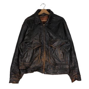 May include: A brown leather jacket with a zipper closure and two large flap pockets. The jacket has a distressed look and is made of a thick, durable leather.