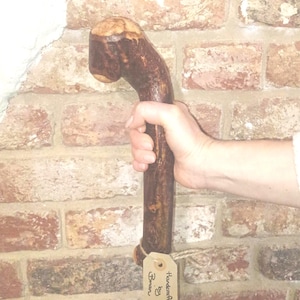 May include: A white ceramic mug with a black handle and the text "But First, Coffee" in a bold, black font. The mug is set against a blurred background. The mug appears to be approximately 10 cm tall.