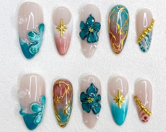 May include: Ten fake nails with a teal and gold design. Some nails have a teal and white ombre effect, others have gold accents, and some have a teal flower design.