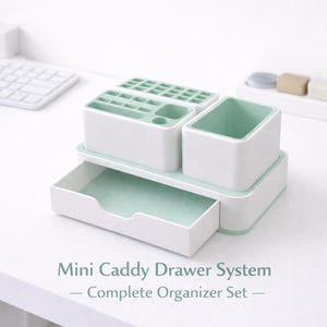 May include: A white and mint green desk organizer with multiple compartments and a pull-out drawer. The organizer includes sections for pens, pencils, and other small items. The text "Mini Caddy Drawer System - Complete Organizer Set" is displayed.