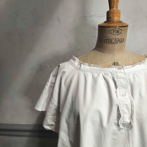 May include: A white cotton nightdress featuring a wide neckline with delicate lace trim, short flutter sleeves, and a front button placket with matching lace detailing. The garment is displayed on a beige mannequin with the text Stockman 40.