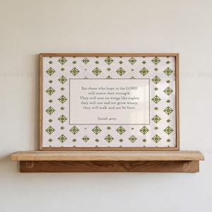 May include: A framed print featuring a repeating green cross-stitch pattern on a white background. The central text reads: But those who hope in the LORD will renew their strength. They will soar on wings like eagles; they will run and not grow weary, they will walk and not be faint. Isaiah 40:31.