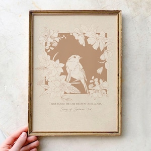 Könnte beinhalten: Ein gerahmter Wandkunstdruck mit beigem Hintergrund und einem zentralen braunen Quadrat, das eine Strichzeichnung eines Vogels umgeben von Blumen zeigt. Der Text lautet: I HAVE FOUND THE ONE WHOM MY SOUL LOVES. Song of Solomon 3:4.