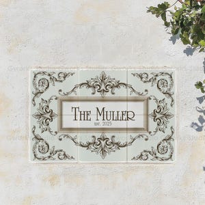 May include: Rectangular ceramic house sign with the name "The Muller" and "Est. 2025" in a decorative font. The sign has a light blue background with ornate brown scrollwork and a light brown border.