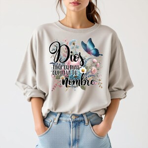 May include: A light gray sweatshirt with a floral design and a butterfly. The text on the shirt reads "Dios tiene un plan que lleva tu nombre".