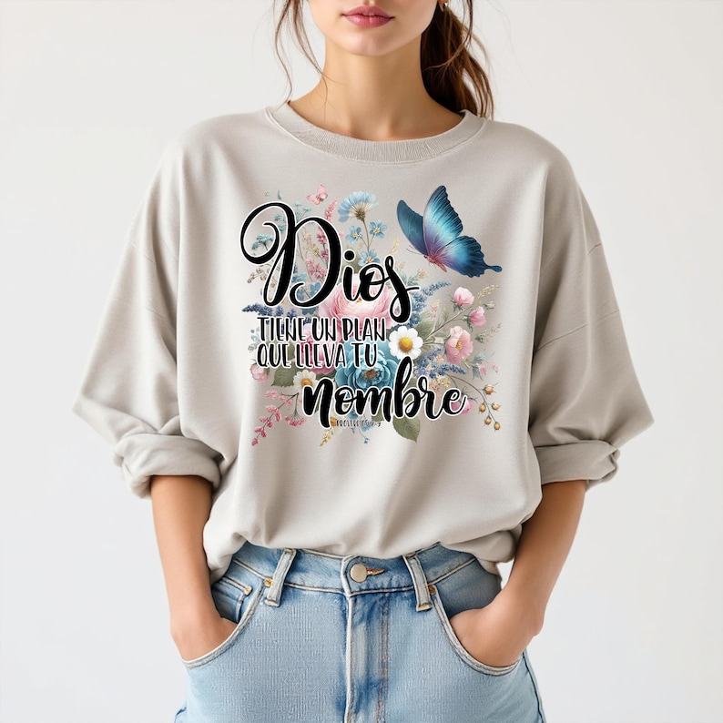 May include: A light gray sweatshirt with a floral design and a butterfly. The text on the shirt reads "Dios tiene un plan que lleva tu nombre".