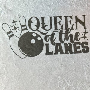 May include: A white t-shirt with black text that reads "Queen of the Lanes" and a graphic of a bowling ball and pins.