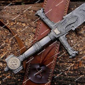 May include: A Damascus steel sword with a patterned blade and an ornate silver-toned metal hilt. The pommel features a circular gold-toned Star of David emblem. The sword rests on a brown leather sheath with visible stitching and leather ties.